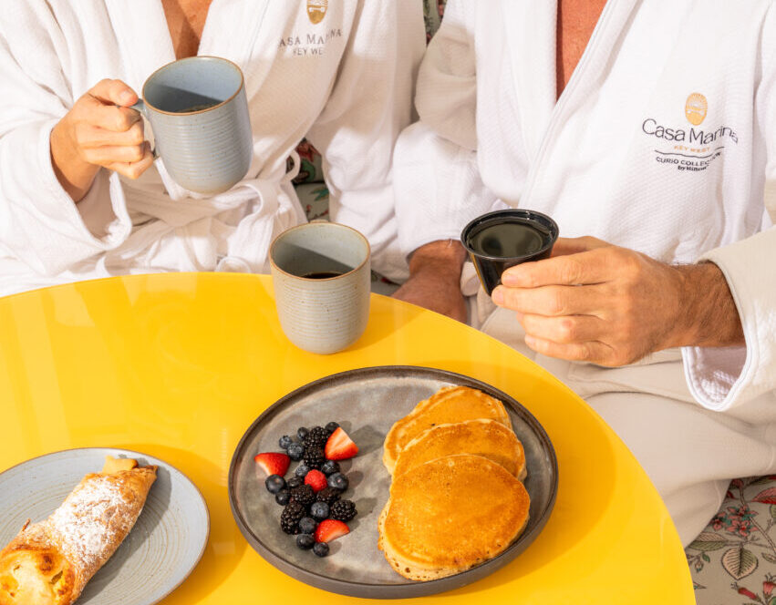 Couple eating breakfast in robes in guest room